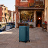 Valise Murano Rio Trunk bleu grisé devant une boutique de souffleur de verre sur l'île de Murano
