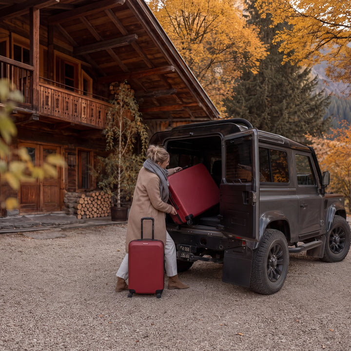 Set de valises Travel World rouge chargé dans un Land Rover Defender devant un chalet de montagne en automne Image