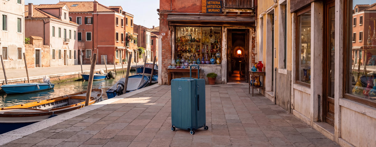 Valise Murano Rio Trunk bleu grisé devant une boutique de souffleur de verre sur l'île de Murano